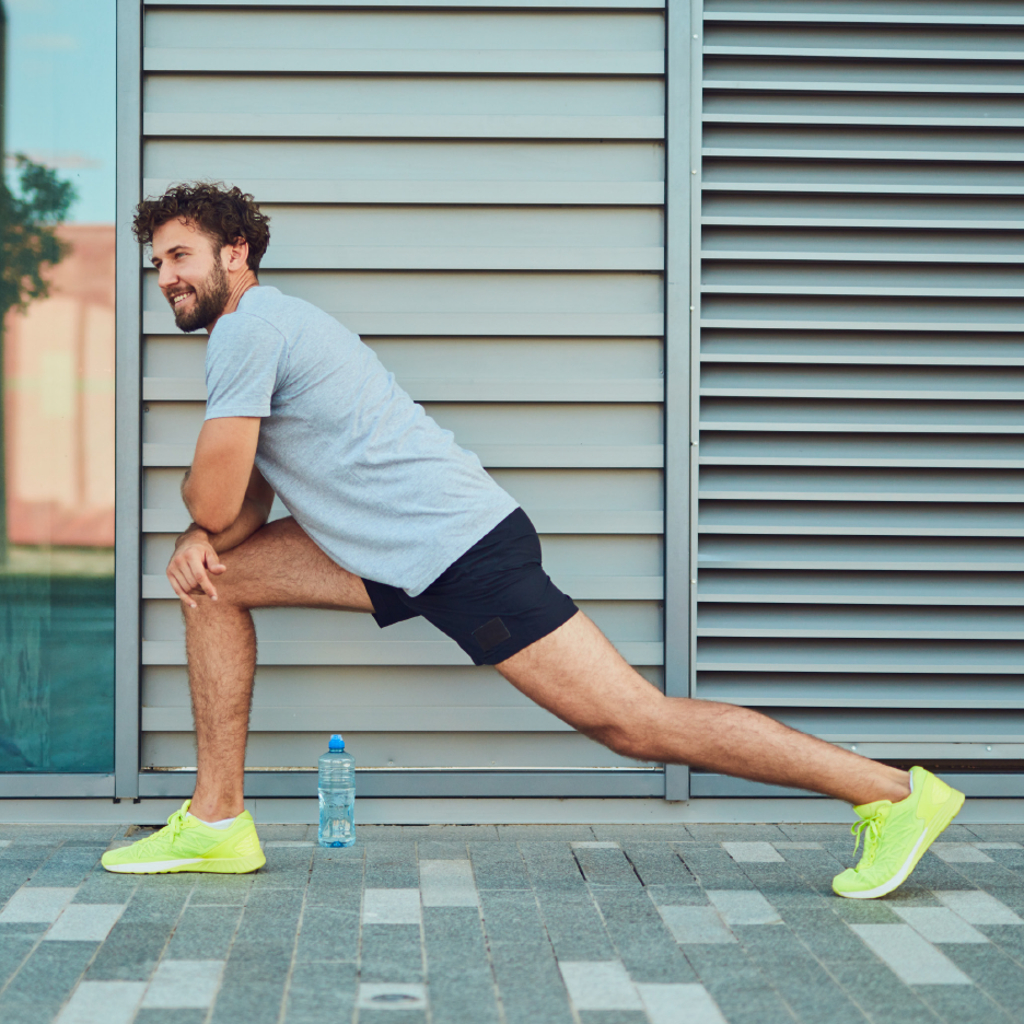 Άνδρας με αθλητικά ρούχα κάνει διατάσεις σε εξωτερικό χώρο με ένα μπουκάλι νερό.