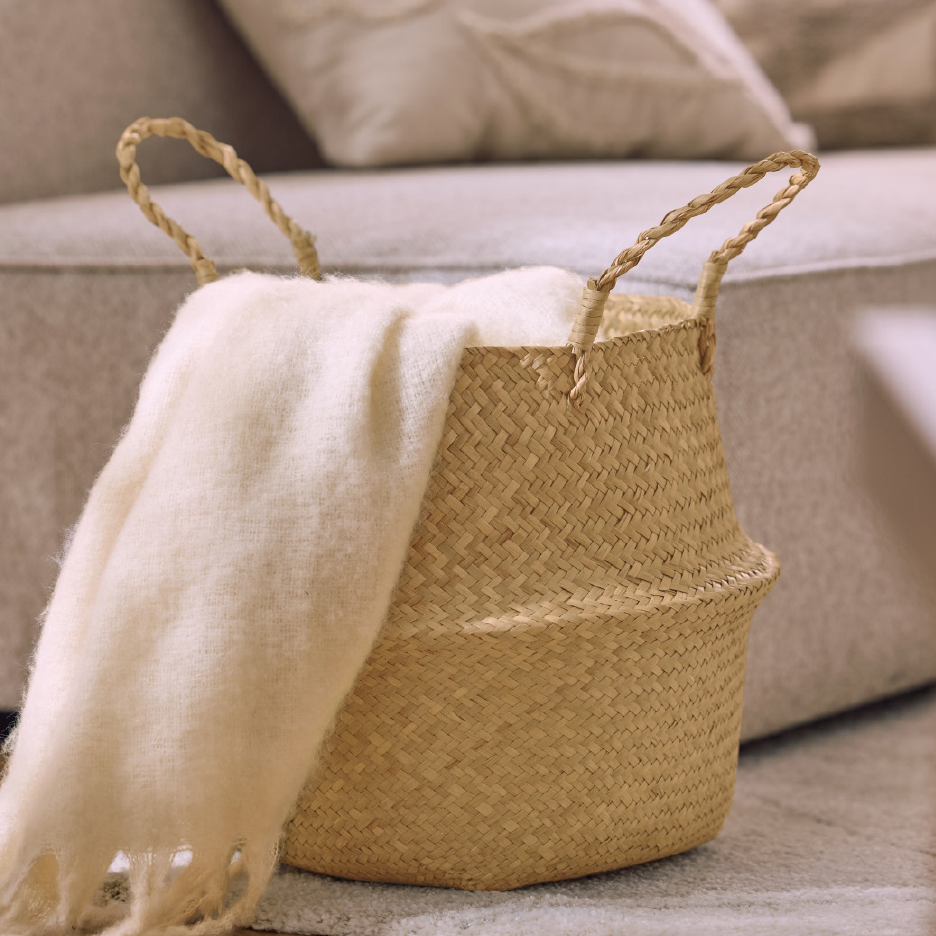 Πλεκτή καλάθα με μια απαλή, κρεμ κουβέρτα, δίπλα σε έναν καναπέ.