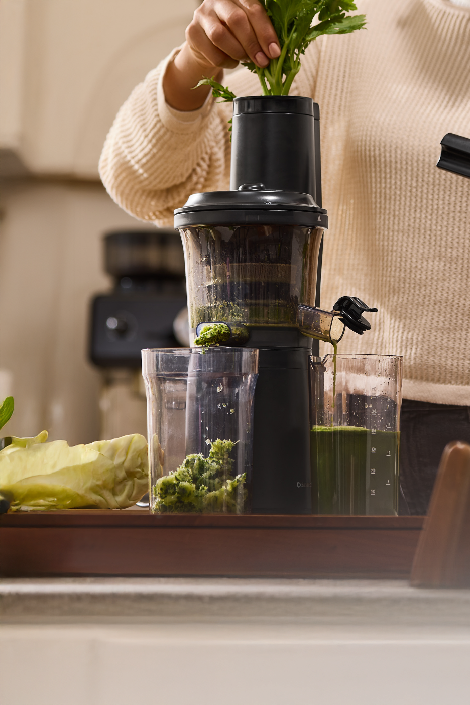 Άτομο στύβει πράσινα λαχανικά με αργό αποχυμωτή, παράγοντας πράσινο χυμό και πολτό.