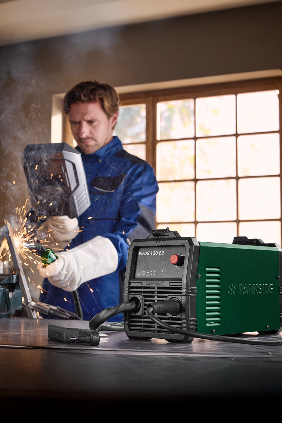 Άνδρας συγκολλά με μια συμπαγή πράσινη και μαύρη μηχανή συγκόλλησης σε πάγκο εργασίας.