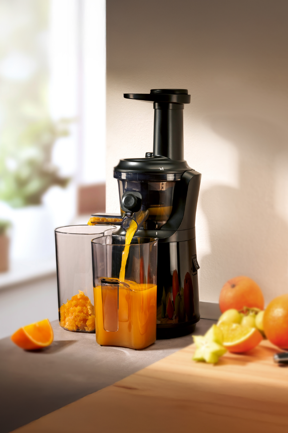 Μαύρος αποχυμωτής φτιάχνει φρέσκο χυμό πορτοκαλιού, με πολτό φρούτων και πορτοκάλια στον πάγκο.