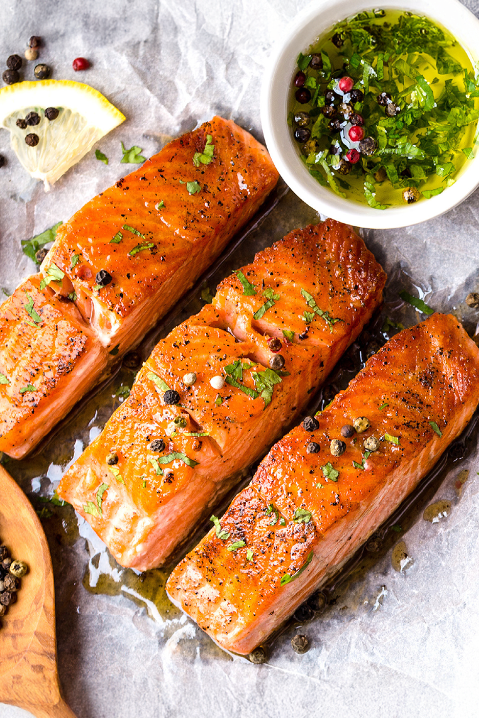 Τρία μαγειρεμένα φιλέτα σολομού με βότανα, μπαχαρικά, λεμόνι και ένα μπολ με πράσινη σάλτσα.