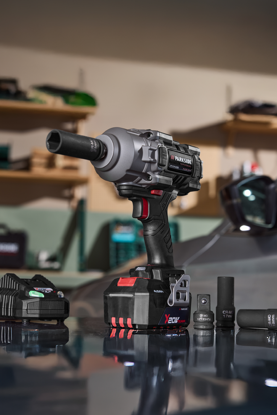 Ασύρματο παλμικό κατσαβίδι με μπαταρία, φορτιστή και διάφορες υποδοχές σε ανακλαστική επιφάνεια.