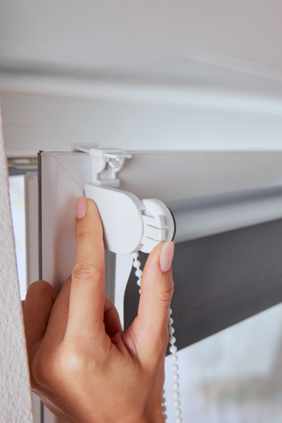 Κοντινό πλάνο ενός χεριού που ρυθμίζει ένα λευκό ρολό περσίδας σε ένα πλαίσιο παραθύρου.