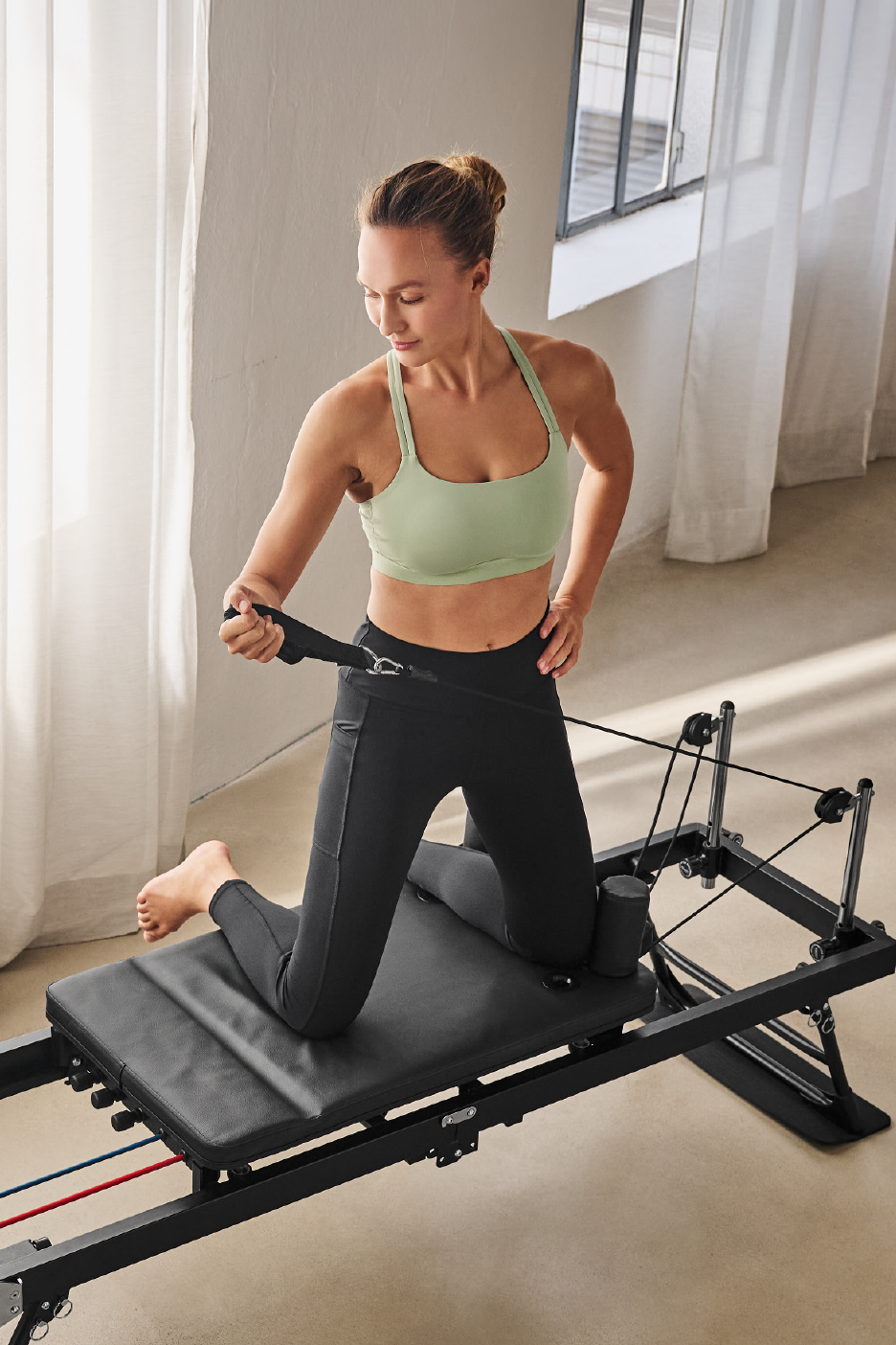 Γυναίκα με αθλητικά ρούχα γυμνάζεται σε reformer Pilates με ιμάντες αντίστασης.