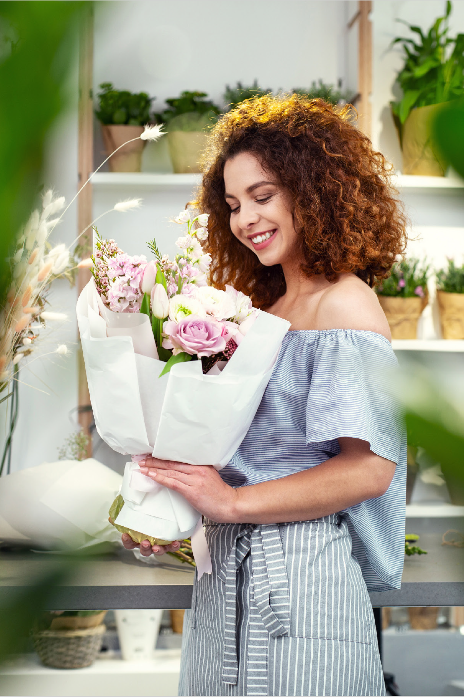 Χαμογελαστή γυναίκα κρατάει μια όμορφη ανθοδέσμη με ροζ και λευκά λουλούδια σε ένα ανθοπωλείο.