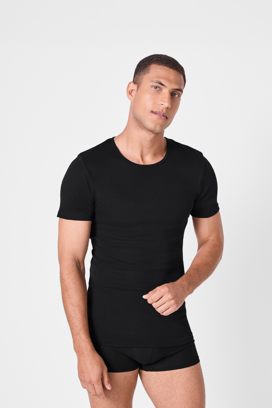 Άνδρας με μαύρο κοντομάνικο μπλουζάκι και μποξεράκι, κοιτάζοντας την κάμερα.