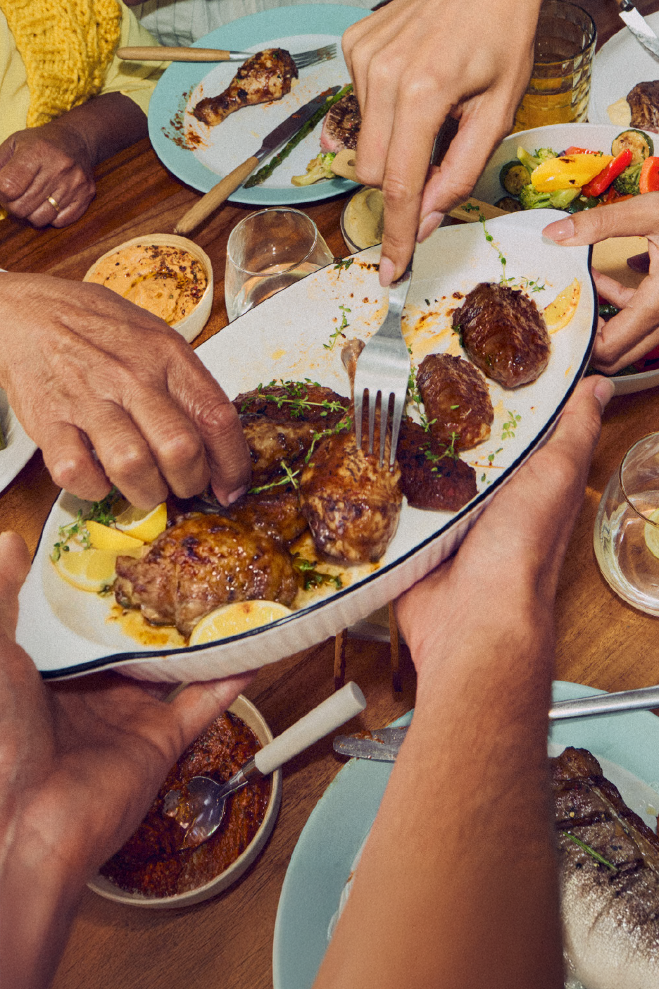 Χέρια σερβίρουν ψητό κοτόπουλο και άλλα πιάτα σε ένα τραπέζι δείπνου.