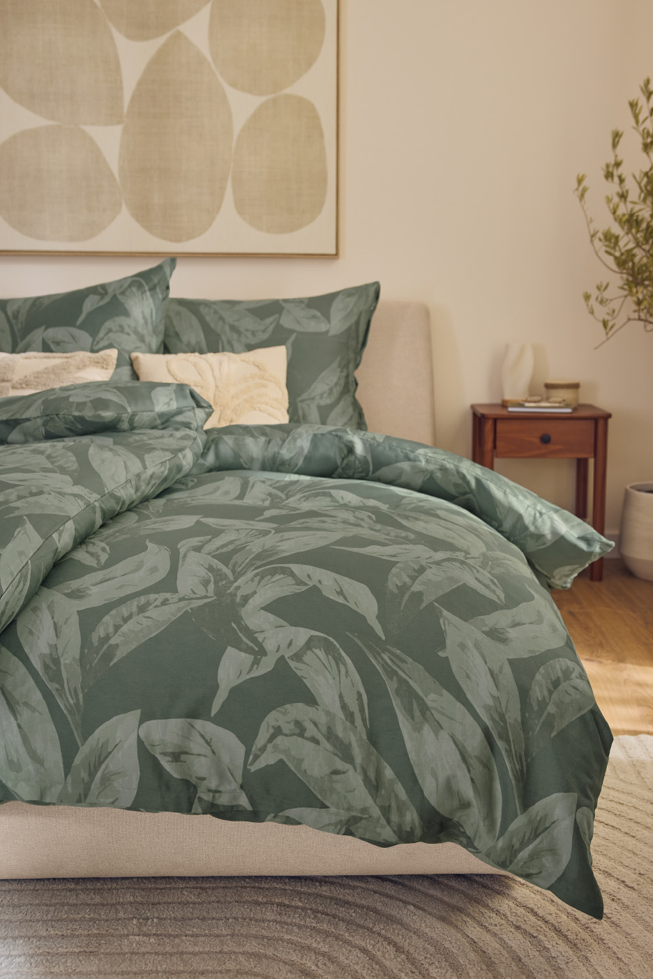 Υπνοδωμάτιο με πράσινο πάπλωμα με σχέδιο φύλλων, μαξιλάρια και κομοδίνο.