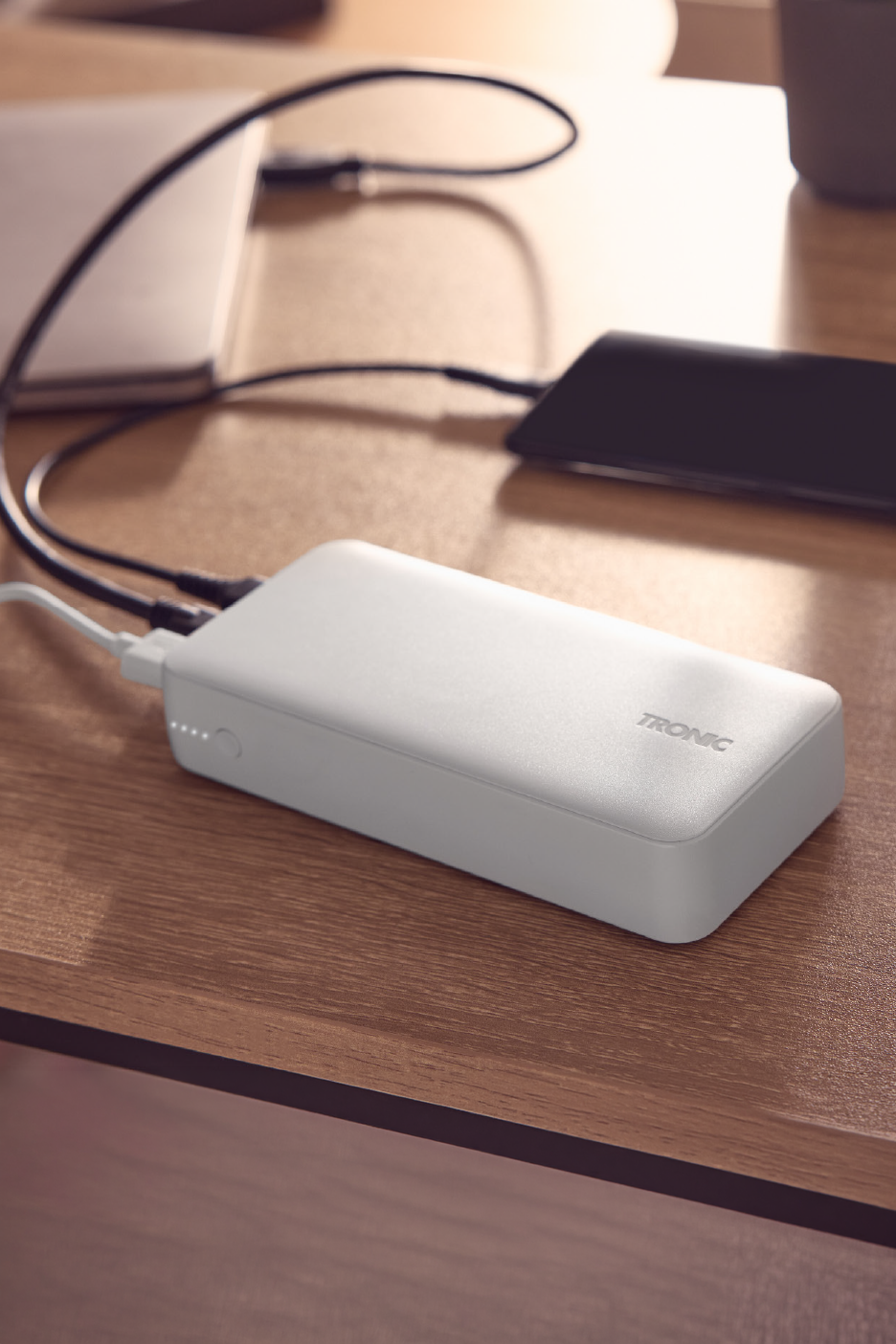 Λευκό power bank φορτίζει ένα laptop και ένα smartphone σε ένα ξύλινο γραφείο.