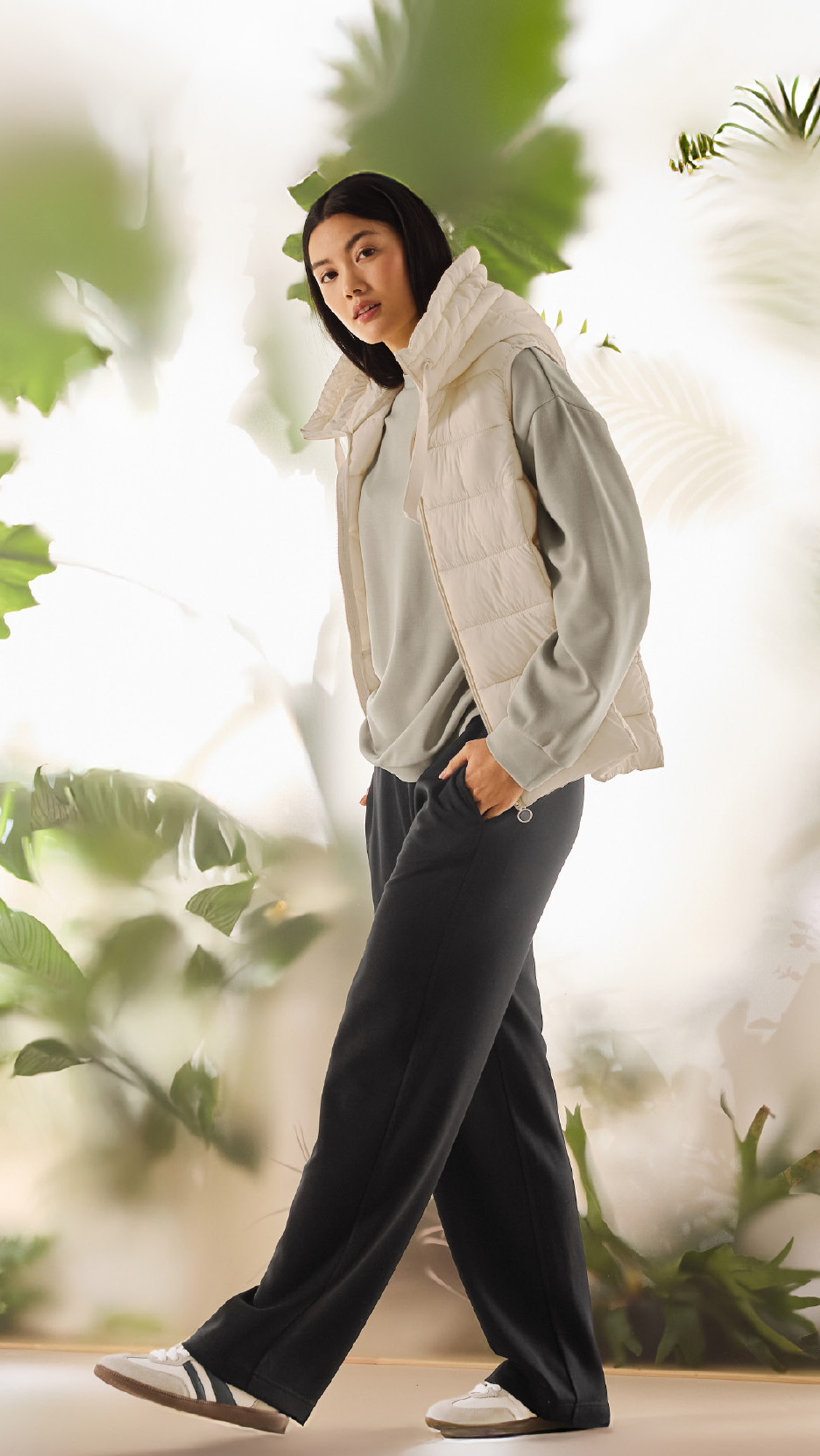 Γυναίκα με κρεμ αμάνικο μπουφάν, ανοιχτό πράσινο φούτερ και μαύρη φόρμα.