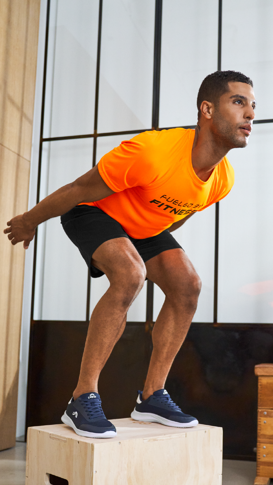 Άνδρας με πορτοκαλί μπλουζάκι και μαύρο σορτς κάνει άλματα σε κουτί, φορώντας μπλε αθλητικά παπούτσια.