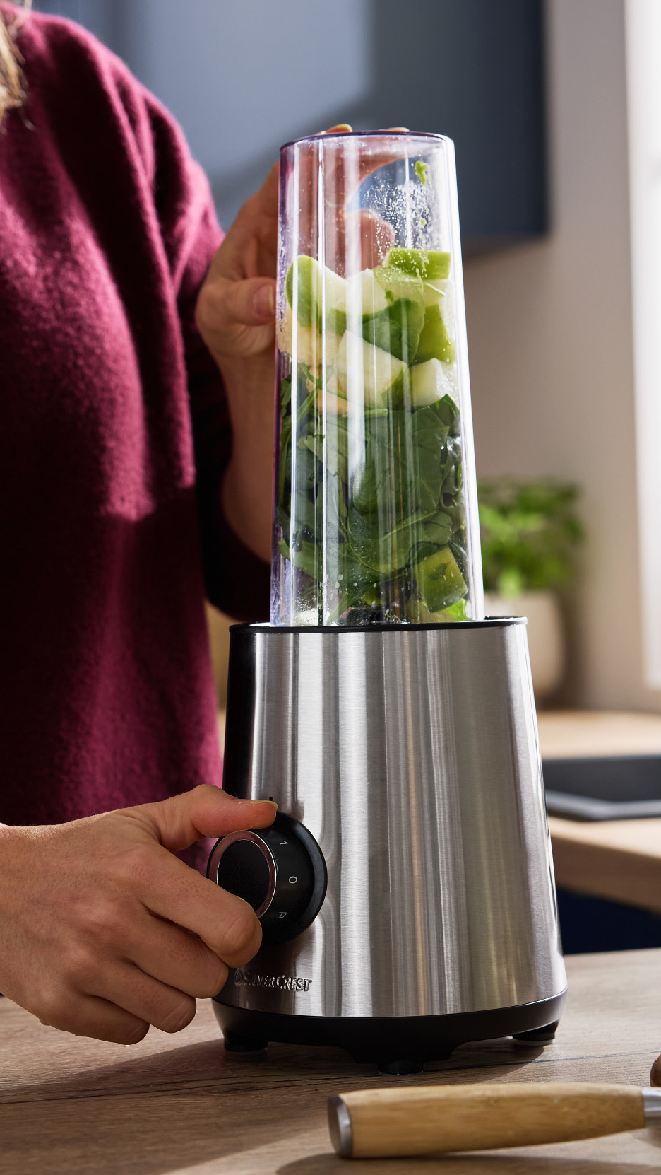 Άτομο που ετοιμάζει ένα πράσινο smoothie σε μπλέντερ με σπανάκι και κομμάτια μήλου.