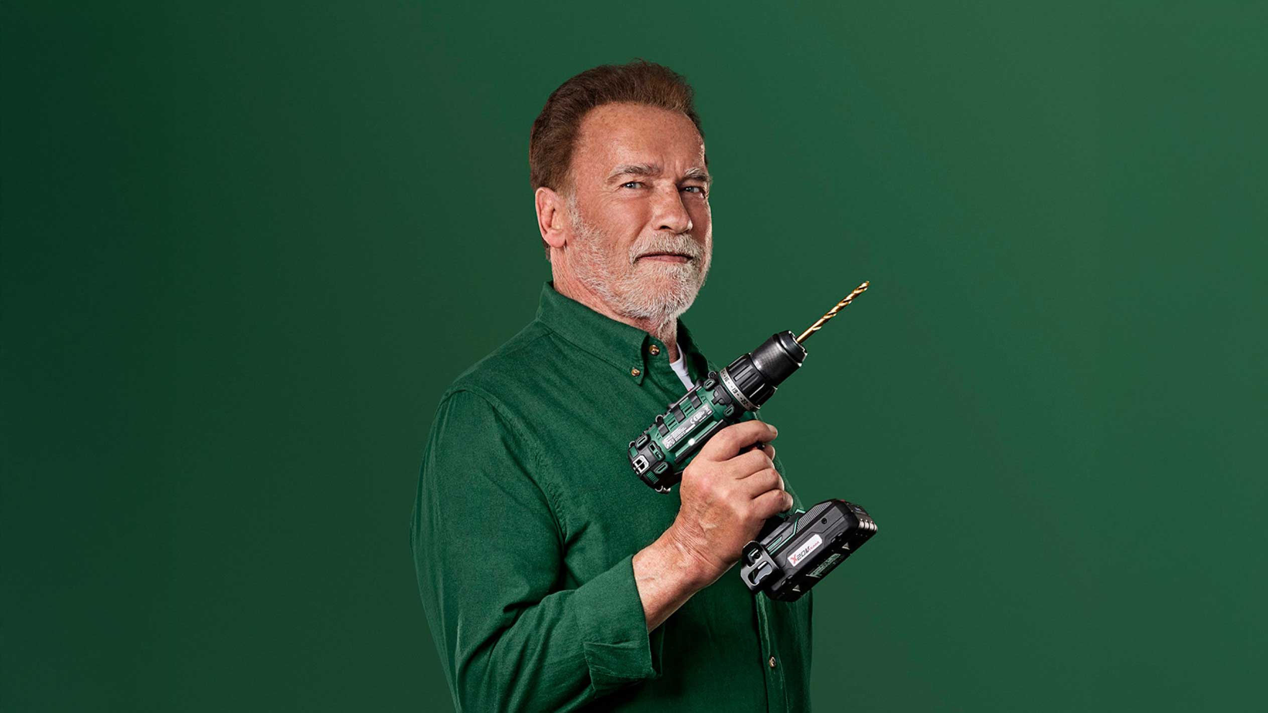 Ο Άρνολντ Σβαρτσενέγκερ κρατά ένα πράσινο ασύρματο δράπανο με χρυσό τρυπάνι.