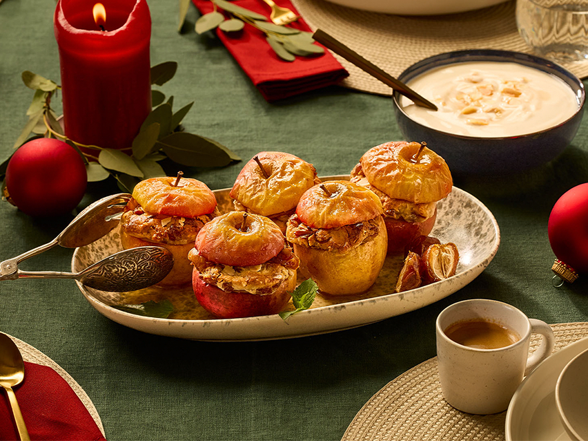 Ψητά μήλα με ξηρούς καρπούς και χουρμάδες σε γιορτινό τραπέζι με κόκκινο κερί.