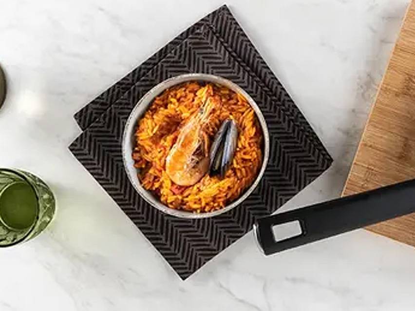 Παέγια θαλασσινών με γαρίδες και μύδια σε ένα μπολ πάνω σε σκούρο σουπλά.