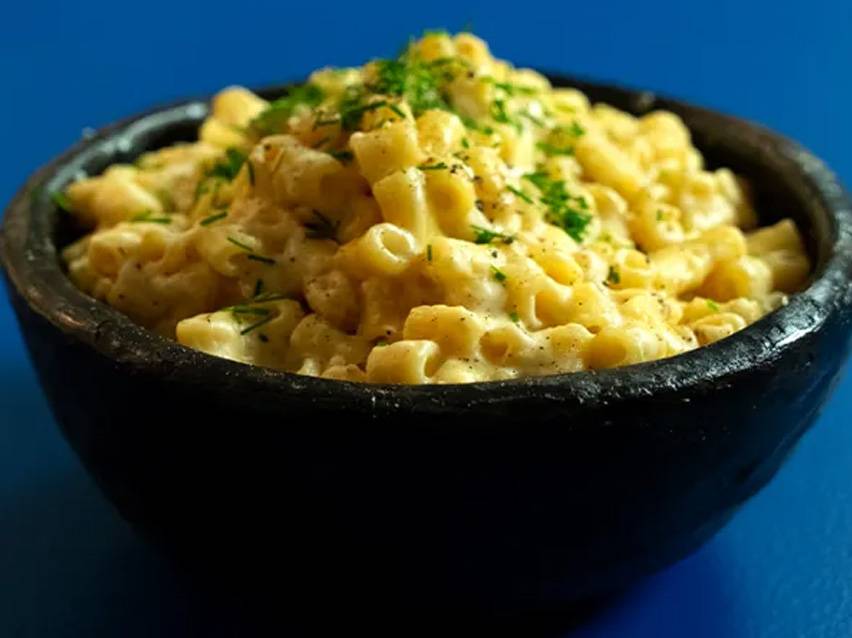 Μακαρόνια με τυρί σε μαύρο μπολ, γαρνιρισμένα με μυρωδικά.