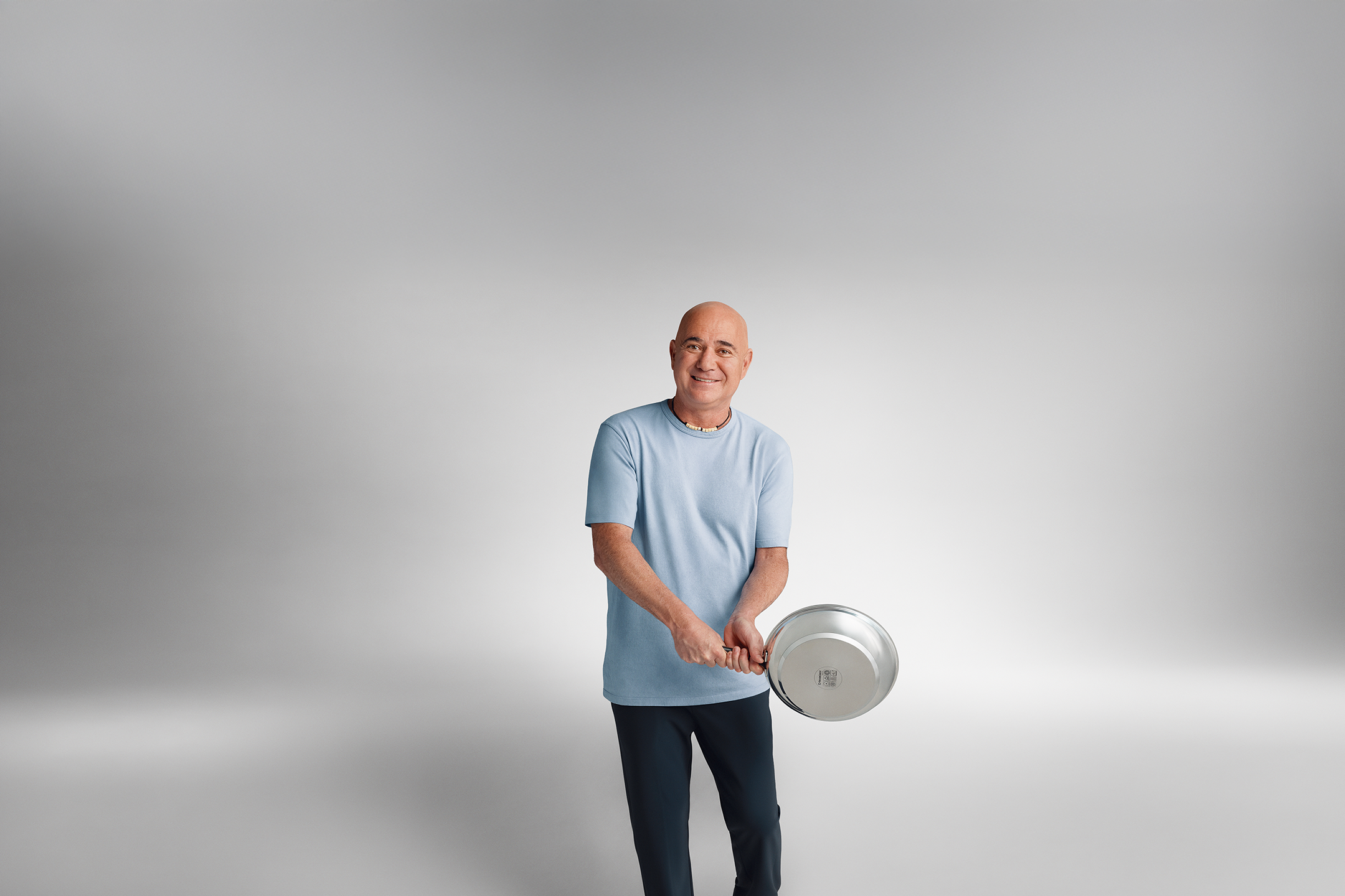 Ο Andre Agassi με ένα μπλε T-shirt κρατά ένα τηγάνι στα χέρια του.
