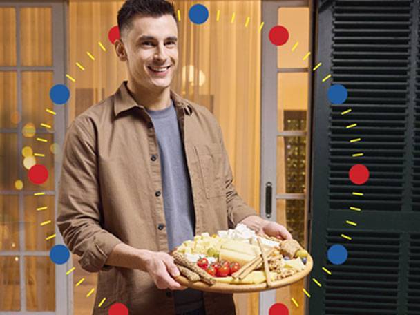 Ένας άντρας κρατάει μια ξύλινη σανίδα με πιάτο τυριών και αλλαντικών.